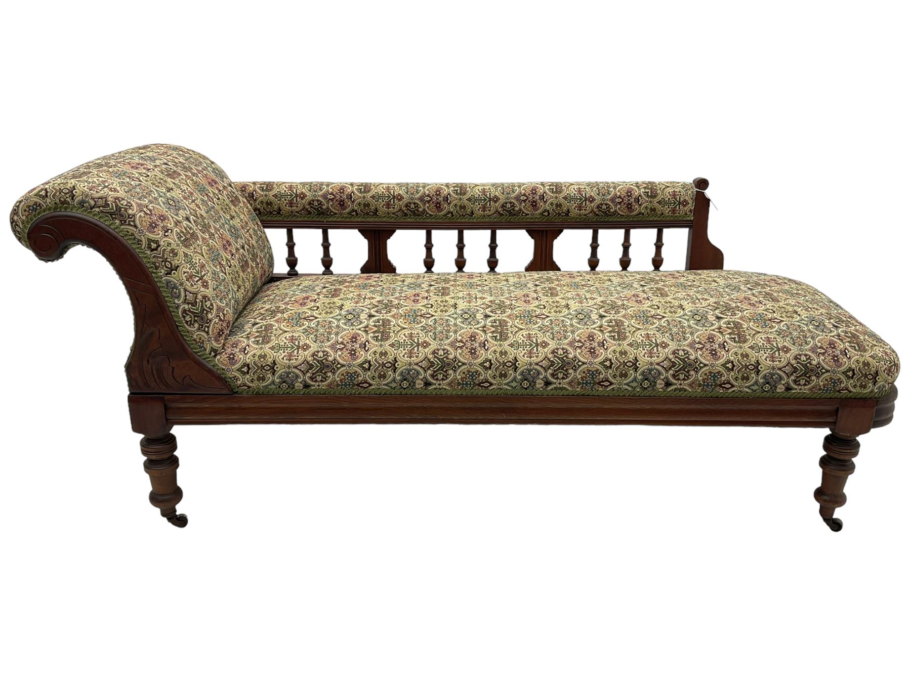 Late 19th century walnut framed chaise longue, upholstered in floral pattern fabric, rolled back rest and turned balustrade back, on turned feet with brass and ceramic castors 