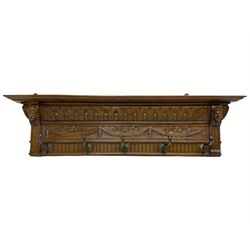 Late 20th century carved oak wall hanging coat rack, projecting moulded lintel over arcade carved frieze, flanked by two carved masks, fitted with five foliate cast hooks