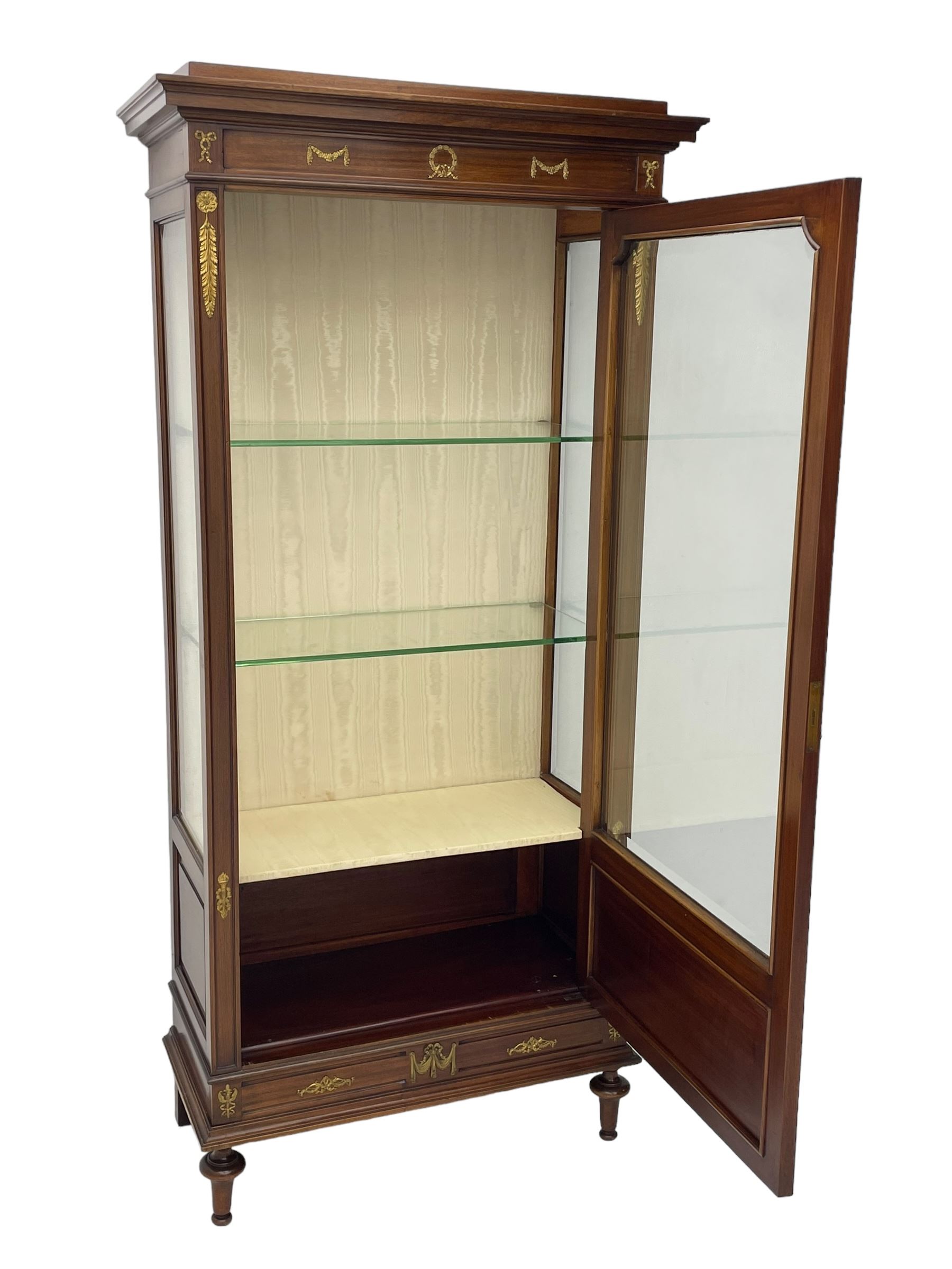 Early 20th century Louis XVI design mahogany vitrine display cabinet, projecting stepped cornice over recessed frieze decorated with gilt metal mounts of festoons and a bellflower wreath, fabric lined interior with two glass shelves, enclosed by bevel glazed door with lower panel, on two turned front feet 