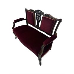 Late Victorian dark oak framed sofa, the backrests, seat and padded arms upholstered in deep red fabric, carved crest rail with scroll and foliate motifs supported by carved uprights, on cabriole supports with leaf carvings terminating in castors