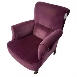 Late Victorian upholstered armchair, in deep purple velvet fabric, buttoned backrest, rolled arms, on splayed back and turned front supports with castors