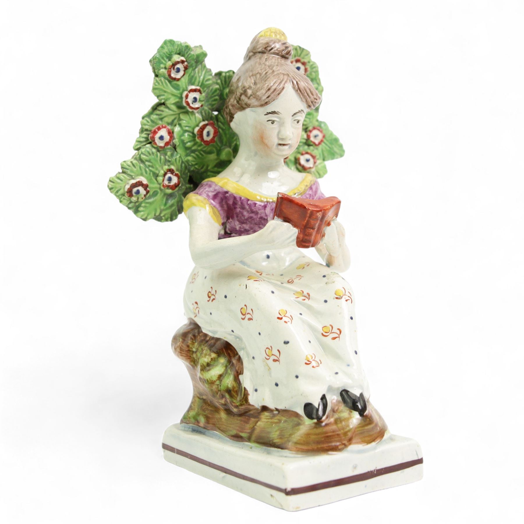 Early 19th century Staffordshire Pearlware figure 'The Reading Girl or Maid' of Obadiah Sheratt type, c1820-1830, modelled as a young woman seated by a tree reading a book, H16cm 