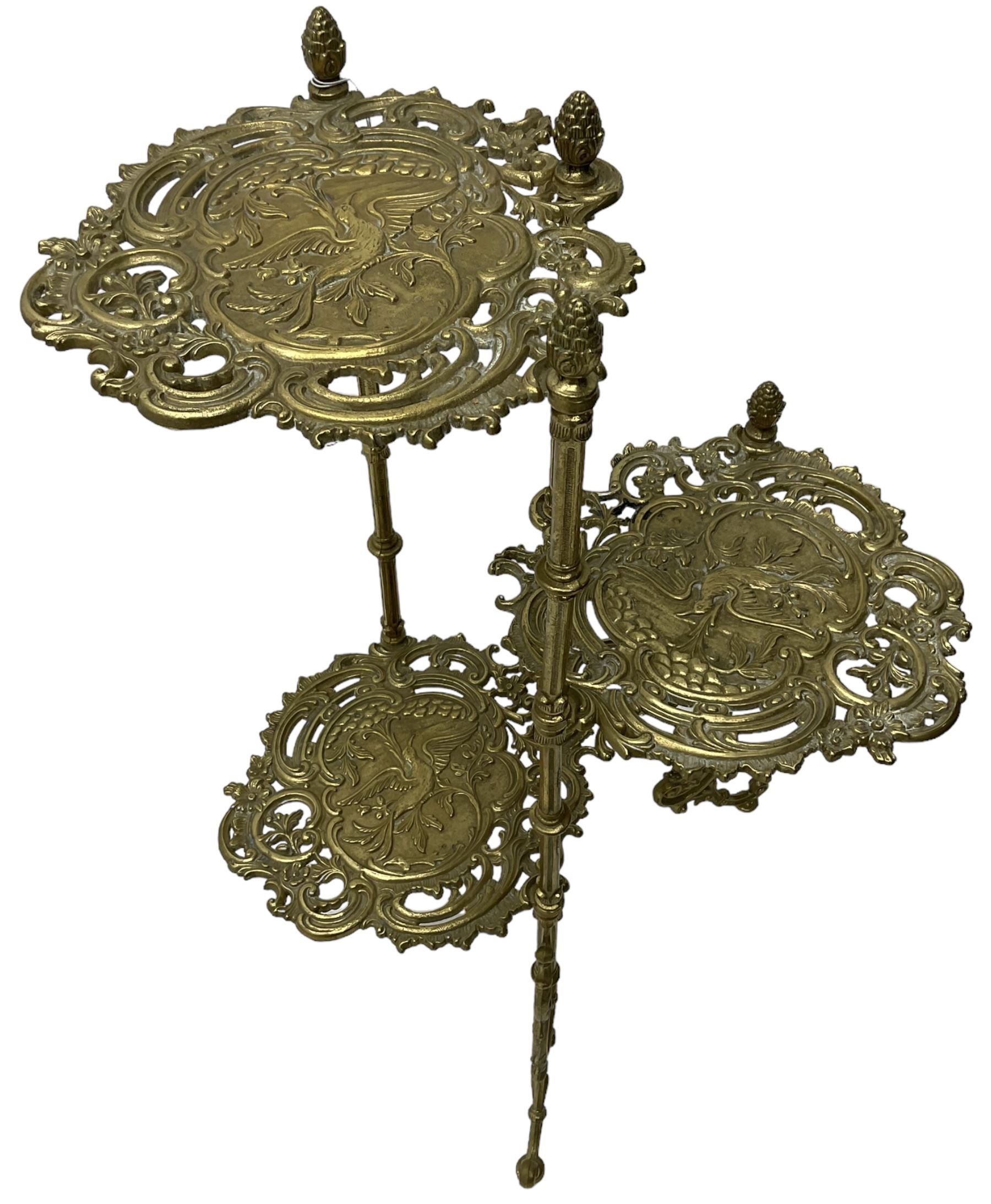 Cast gilt metal three-tier cake stand, each tier decorated with cast foliage scrolls and flower heads with a central bird motif, on turned and fluted supports with splayed C-scroll feet