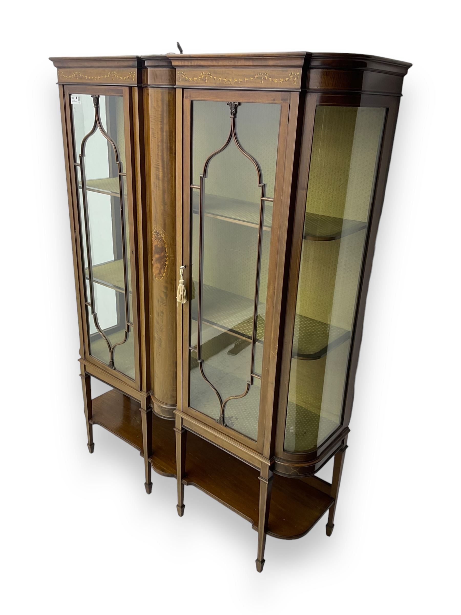 Edwardian inlaid mahogany display cabinet, projecting moulded cornice over two glazed doors, flanked by curved glazed sides and central arched panel with floral medallion, raised on square tapering supports with spade feet united by undertier