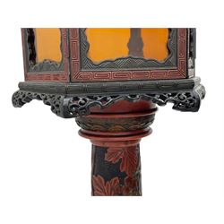 20th century Chinese black and red lacquered hardwood lantern stand, hexagonal shaped canopy top carved with flower heads and scrolls, the lantern fitted with amber tinted glass panes, pierced and carved upper panels, enclosed by two hinged doors, turned stem carved in relief with trailing vine leaves with fruits, stepped hexagonal base with carved decoration  