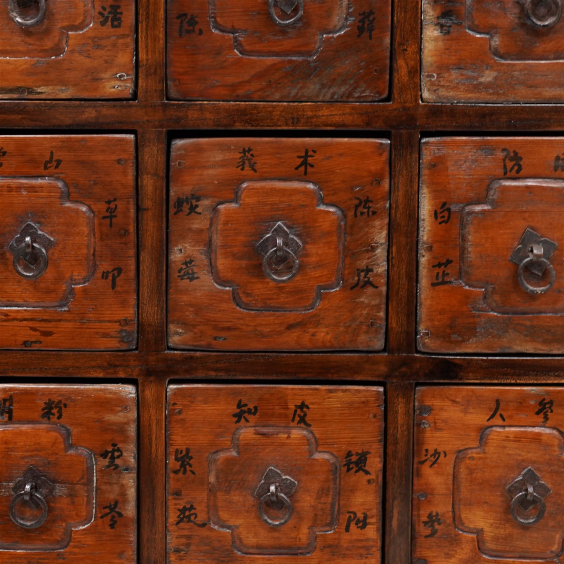 Early 20th century Chinese lacquered elm storage or spice chest, rectangular top with moulded edge, fitted with an assortment of twenty-eight drawers with wrought metal fittings, the facias etched with faux panels and painted with Chinese characters primarily relating to various spices and herbs, on stile feet