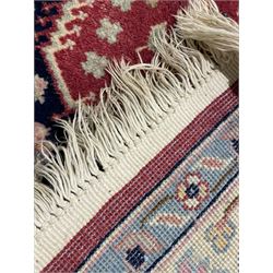 Persian design crimson ground rug, the field decorated with tree of life and floral motifs, enclosed by indigo spandrels with stylised flower head decoration, repeating scrolling border 