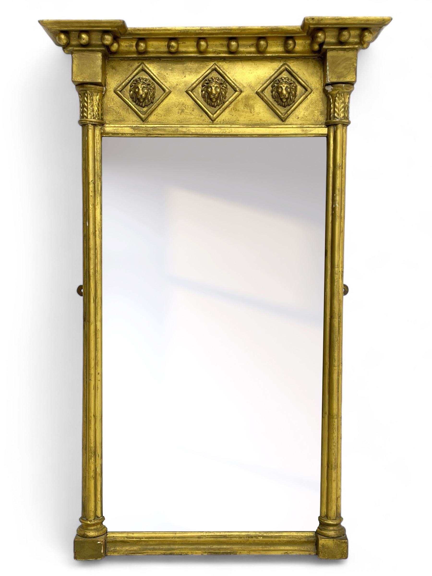 Regency giltwood and gesso pier mirror, projecting moulded cornice with globular mounts, the frieze decorated with three lion masks within lozenges, cluster column uprights with leaf decorated capitals, bevelled mirror plate