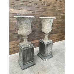 Pair of Georgian design cast stone garden urns, egg and dart rim with raised floral motifs, pedestal base terminating on square plinth, raised on square block plinth