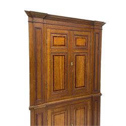 George III and later oak and mahogany banded corner cupboard, moulded cornice over four panelled doors, the door panels inlaid with mahogany bands, projecting square pilasters throughout with applied reeded mouldings, the painted interior fitted with shaped shelves, on moulded plinth base 