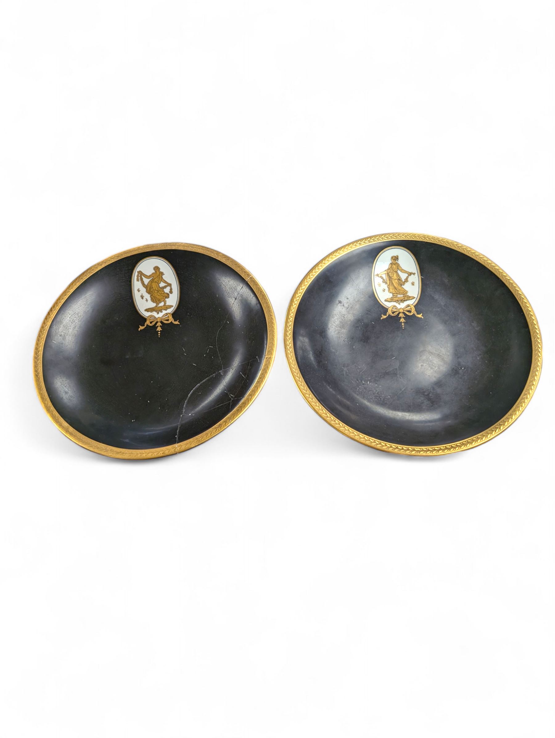 Pair of early 20th century Wedgwood tazzas, the black bowls with gilt foliate borders and painted in gilt with a classical female figure, with retailers mark for Phillip's Ltd Bond Street and printed maker's mark beneath, H6cm, D23.5cm