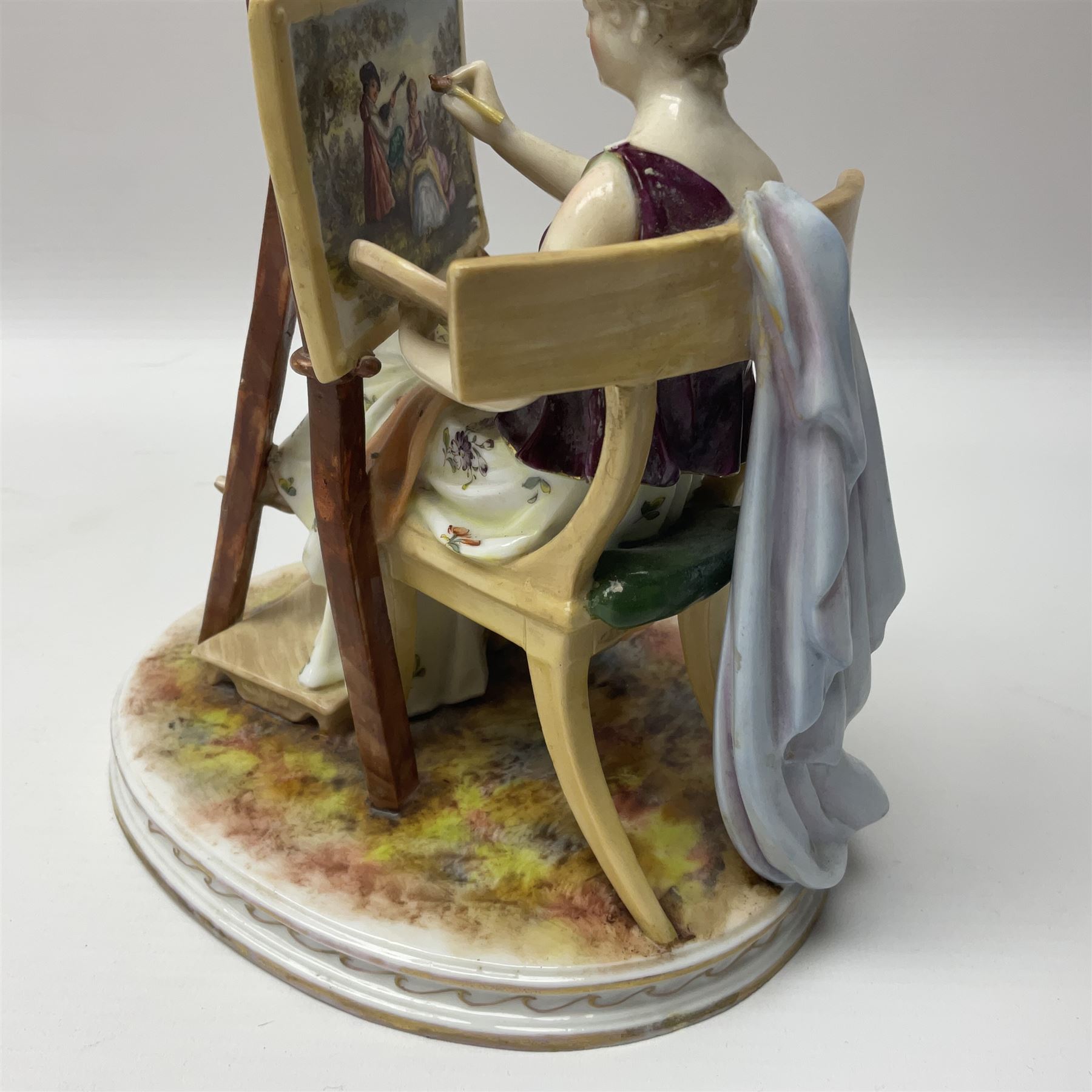 Pair of late 19th/early 20th century Naples figures modelled engaged in the arts, the first example modelled as a female figure seated before an easel, painting a figural scene, the second modelled as a female figure seated before a bust with scultping tools in hand, each upon an oval base with naturalistic painted ground, each with blue crowned N mark beneath, each approximately H16cm, including base L15xm
