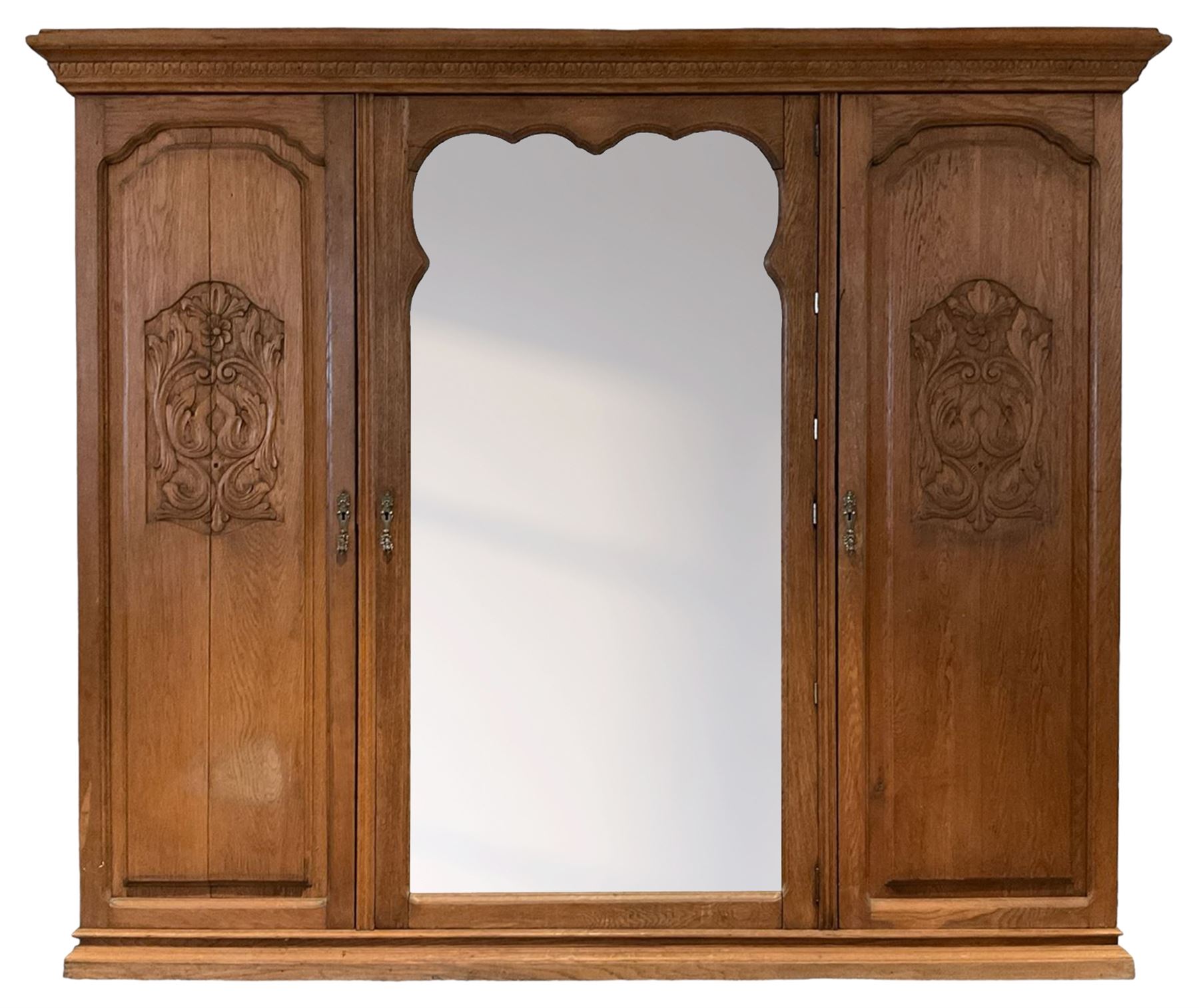 Late 19th century oak triple wardrobe, wide central bevelled mirror door, flanked by two panelled doors each carved with scrolling leaves and flower heads, on moulded skirt base 