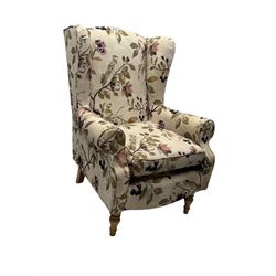 Hardwood-framed wingback armchair, upholstered in cream floral pattern fabric, on turned front feet