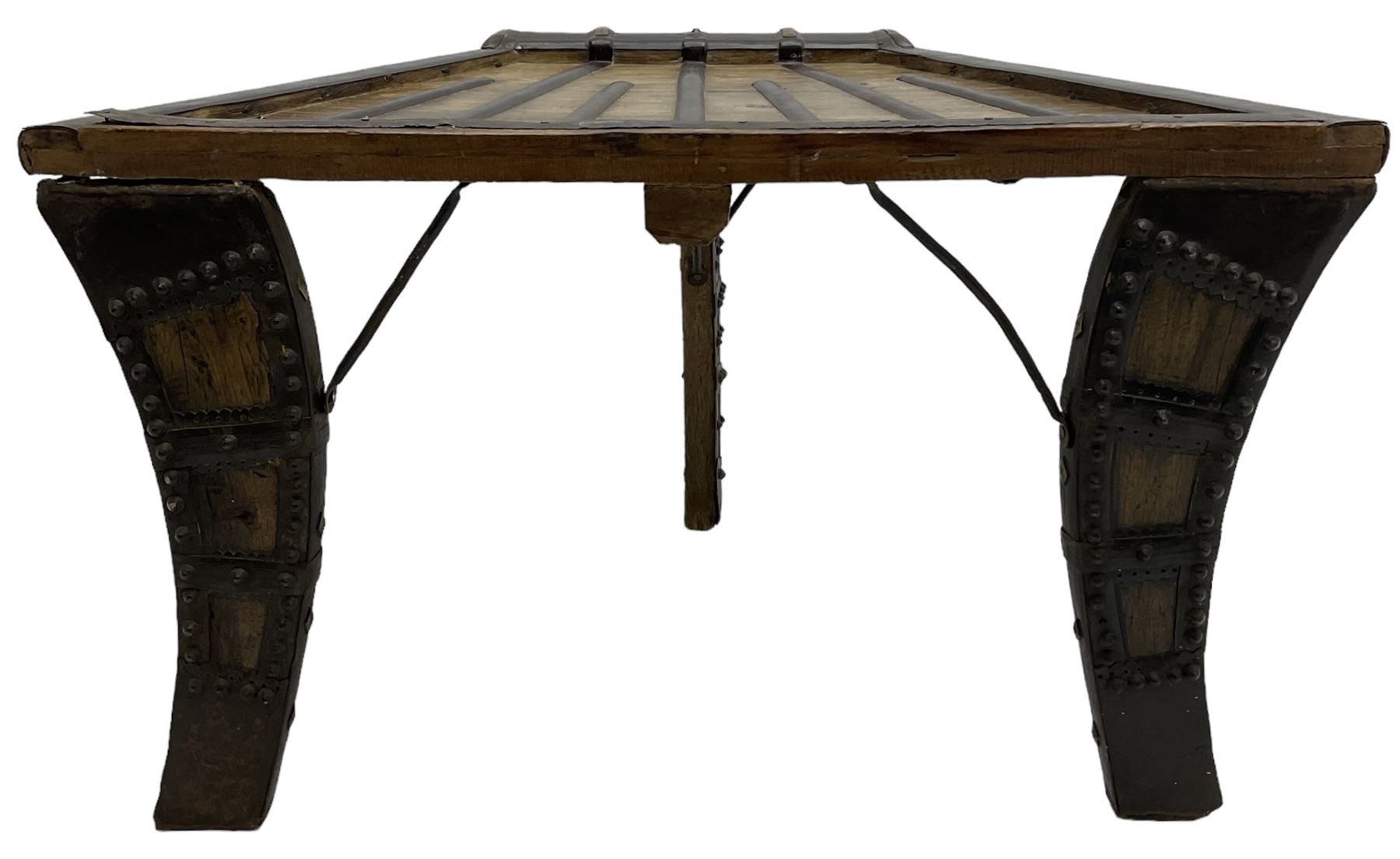 19th century Indian bullock / ox cart converted coffee table, trapezoidal top with applied metal decoration and iron stretchers, raised on three swept supports with stud decoration