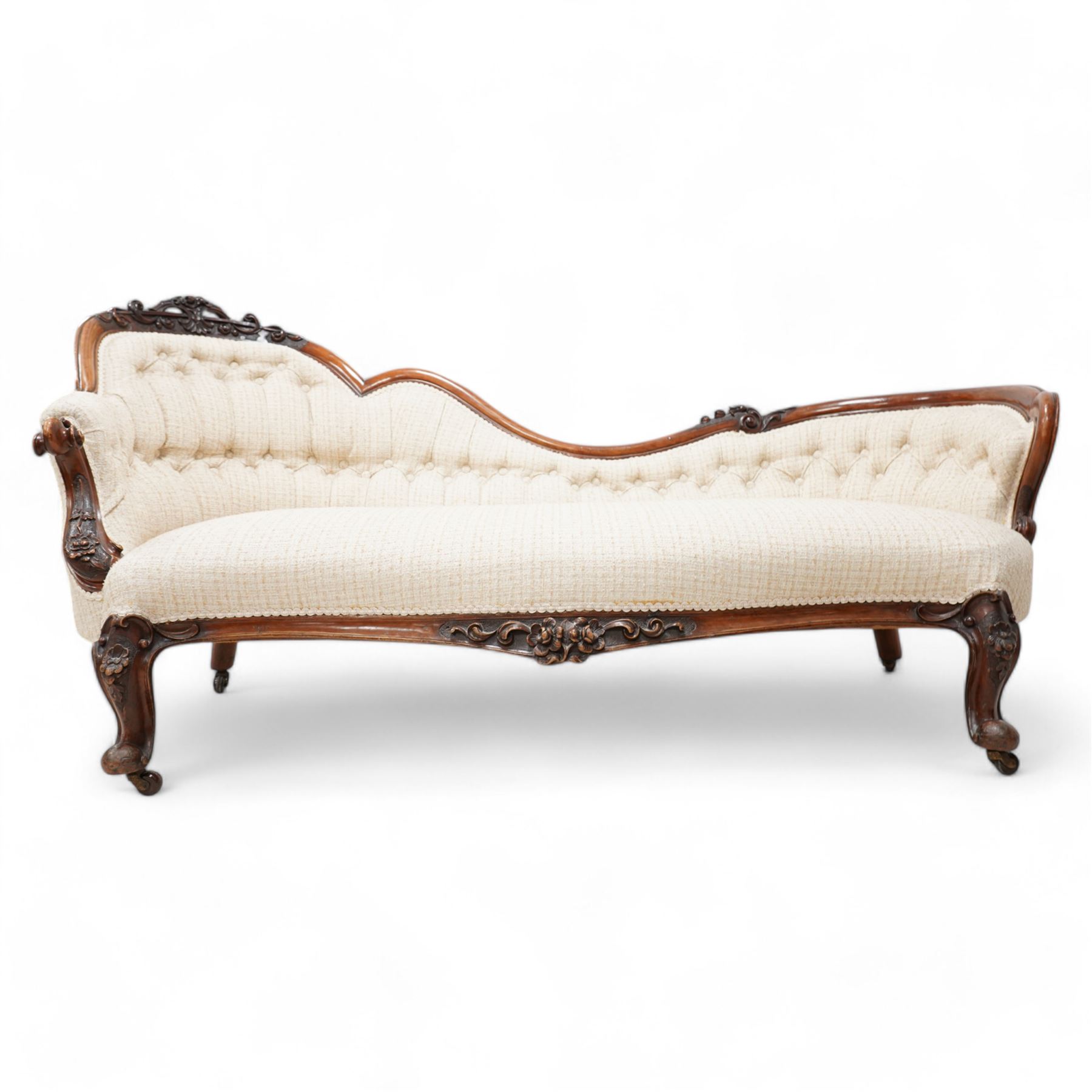 Victorian walnut framed chaise longue, the shaped frame carved with scrolls and flower heads, upholstered in buttoned textured cream fabric, the shaped seat rail carved with flower heads and extending foliate scrolls, on floral carved cabriole feet with castors 