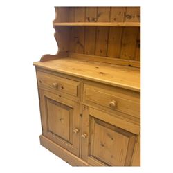 Large traditional pine dresser, shaped cornice over three open shelves, base fitted with four drawers above four panelled cupboards, each with turned wooden knobs, on plinth base