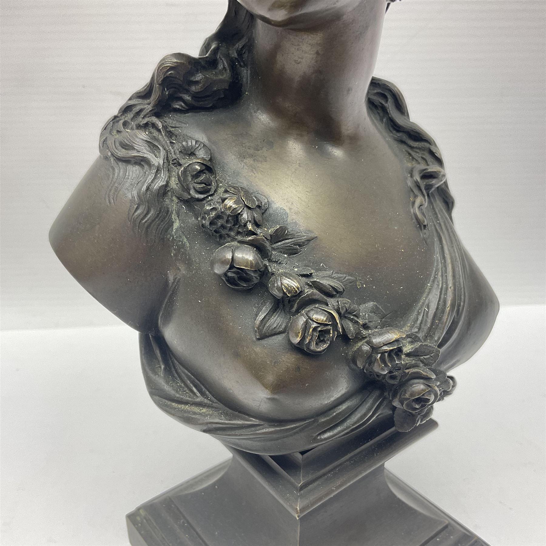 Bronze bust, modelled as a maiden in classical drapery and adorned with floral swags, upon a fluted socle base, overall H23.5cm