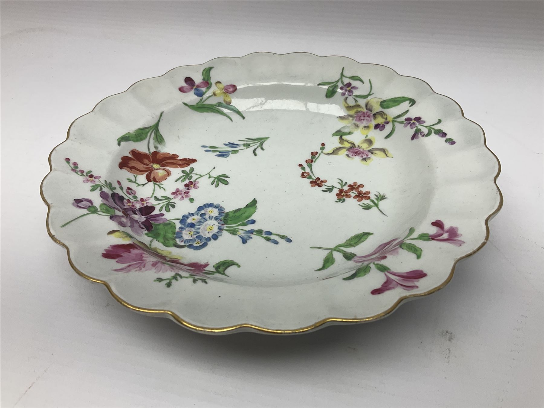 Three 18th century Worcester desert dishes, the first example decorated in the Scarlet Japan pattern, circa 1790, painted with alternating panels of Kakiemon style prunus blossom and chrysanthemum, and orange ground panels with gilt fret detail, D19cm, the second example, circa 1770, decorated with Kakiemon style chrysanthemums and foliage within shaped reserves upon a blue scale ground, with fretted square pseudo mark beneath, D19cm, and the third, circa 1770, painted with polychrome floral sprays and sprigs, D20cm