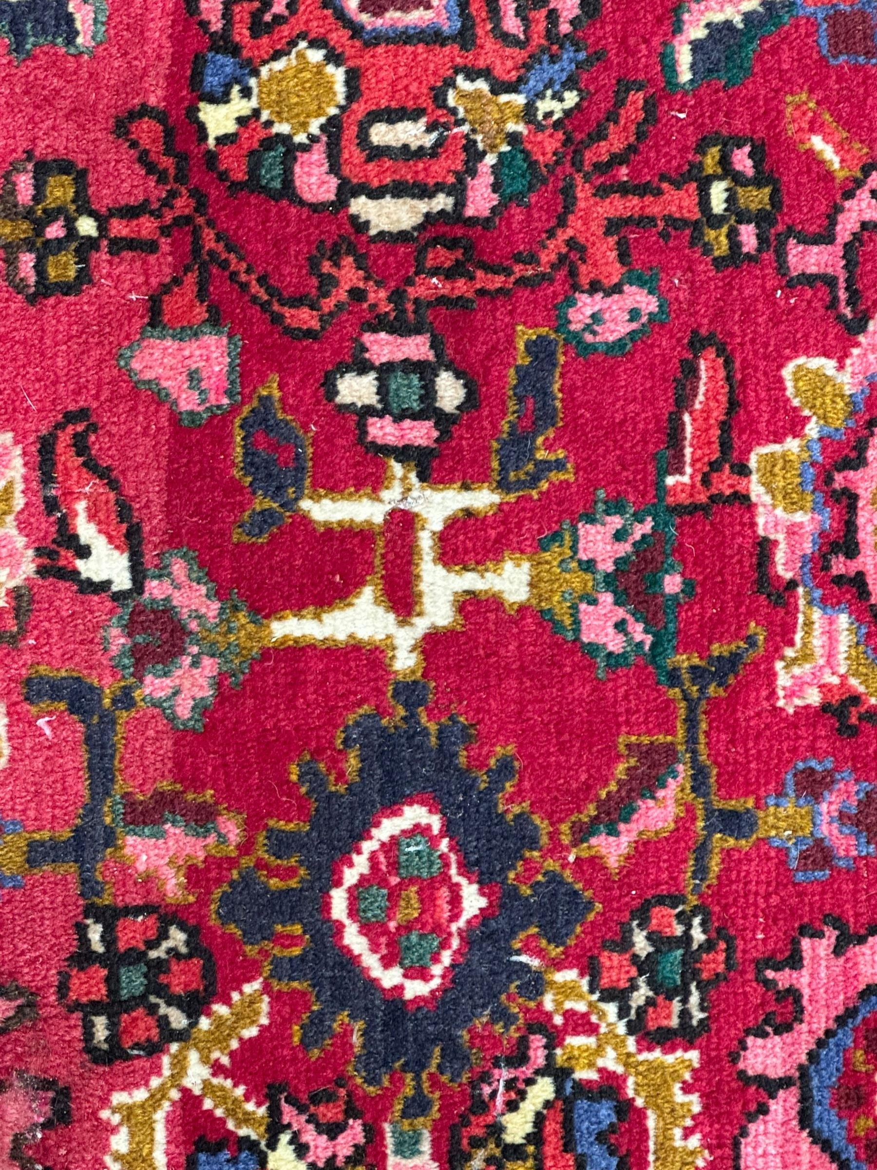 Persian Nanaj crimson ground carpet, the busy field filled with interconnecting stylised plant motifs with scrolling branches, the guarded indigo border decorated with repeating palmettes and foliate patterns