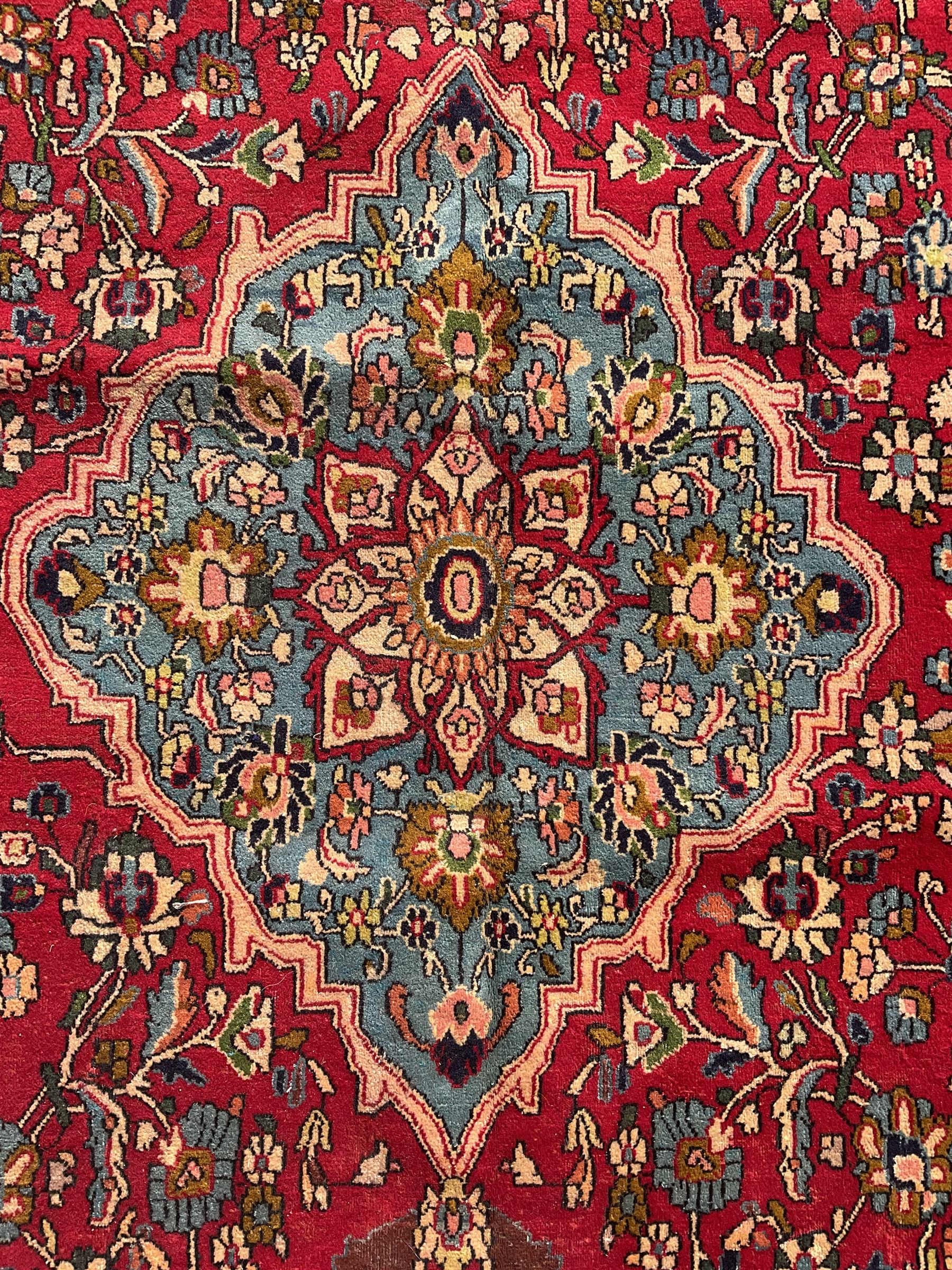 Central Persian Isfahan crimson ground carpet, central floral medallion in ivory and blue, set within a field of dense floral patterns, bordered by a navy band decorated with stylised flower heads and vines