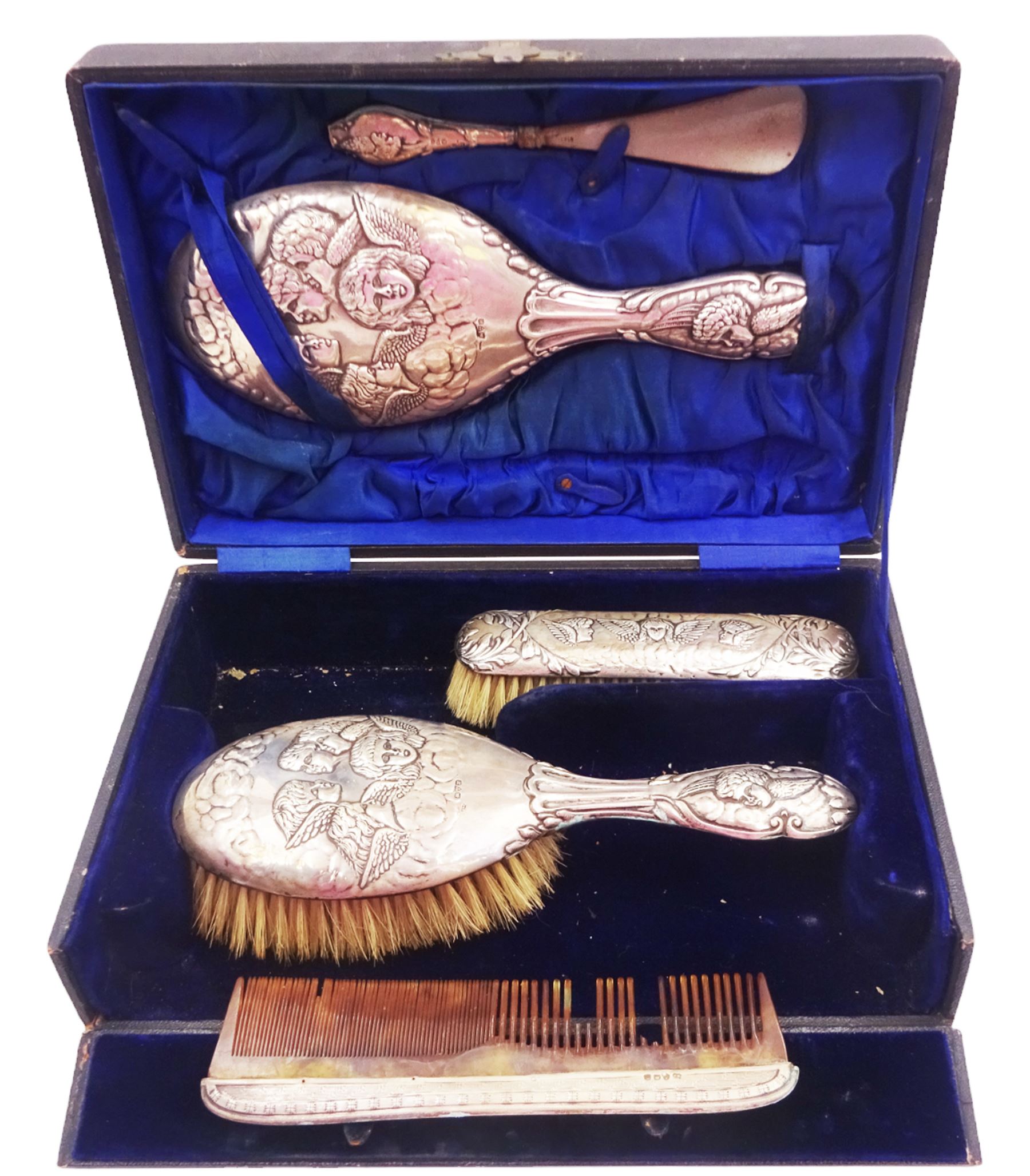 Four piece Edwardian silver mounted dressing table set, comprising hair brush, hand mirror, shoe horn and clothes brush, each embossed with cherubs, hallmarked Chester 1908, makers mark indistinct, together with a silver comb holder, hallmarked, contained within tooled leath, silk and velvet lined fitted case, 