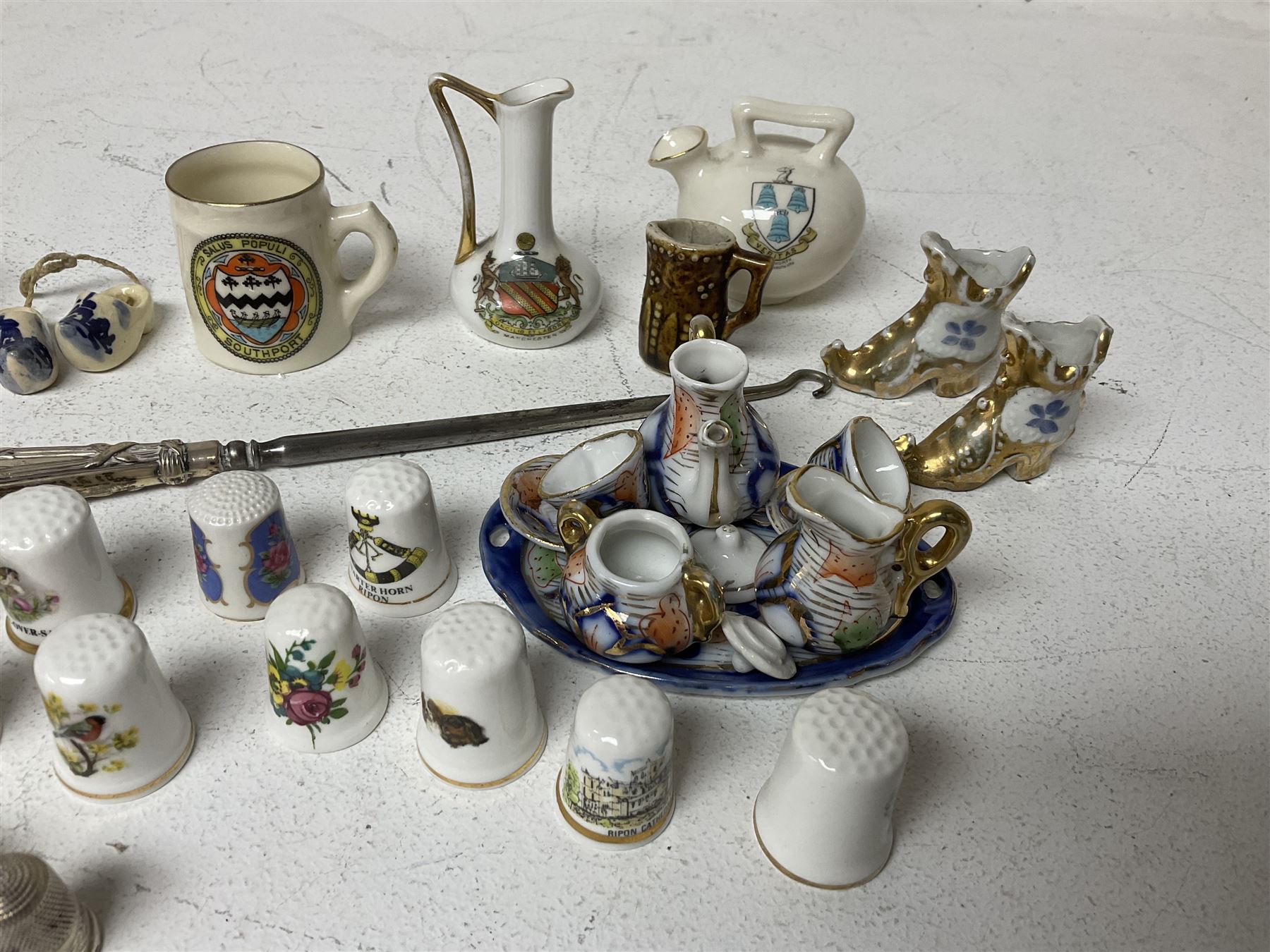 Three hallmarked silver thimbles, a hallmarked silver handled button hook, crested ware including items by W.Goss, miniature oriental style tea set and a collection of ceramic souvenir thimbles