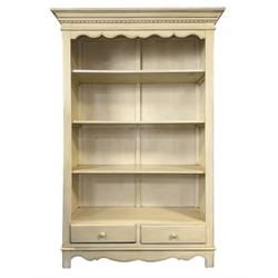 Provincial style cream painted bookcase, projecting cornice over dentil moulding, scalloped frieze above three open shelves, lower section fitted with two drawers, on bracket feet with apron