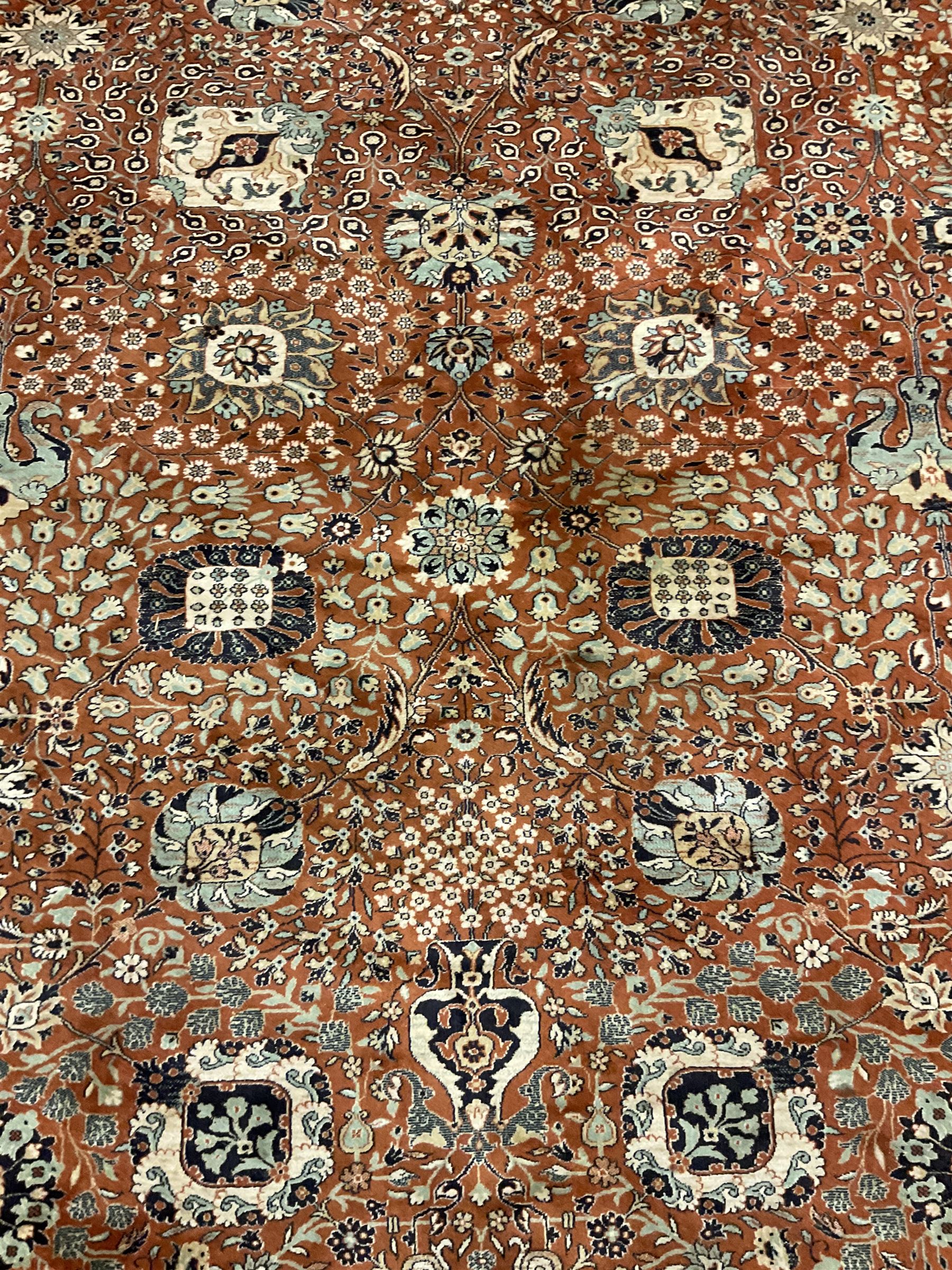 Persian design carpet, rust ground field decorated with large stylised plant motifs surrounded by smaller floral motifs, repeating trailing border