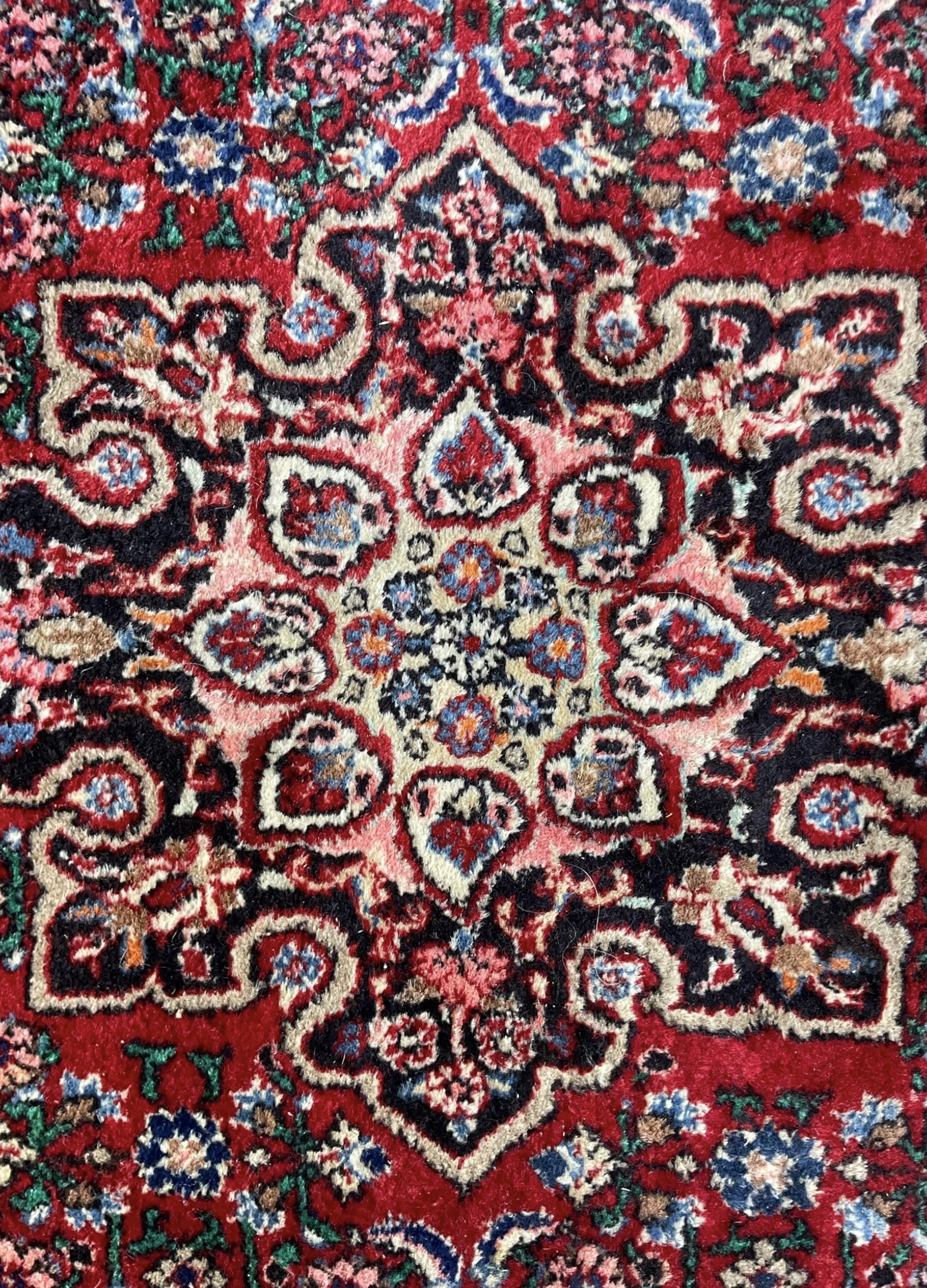 Persian design crimson ground rug, the field decorated with central floral pole medallion and surrounded by foliate patterns with matching spandrels, guarded border with repeating palmette motifs