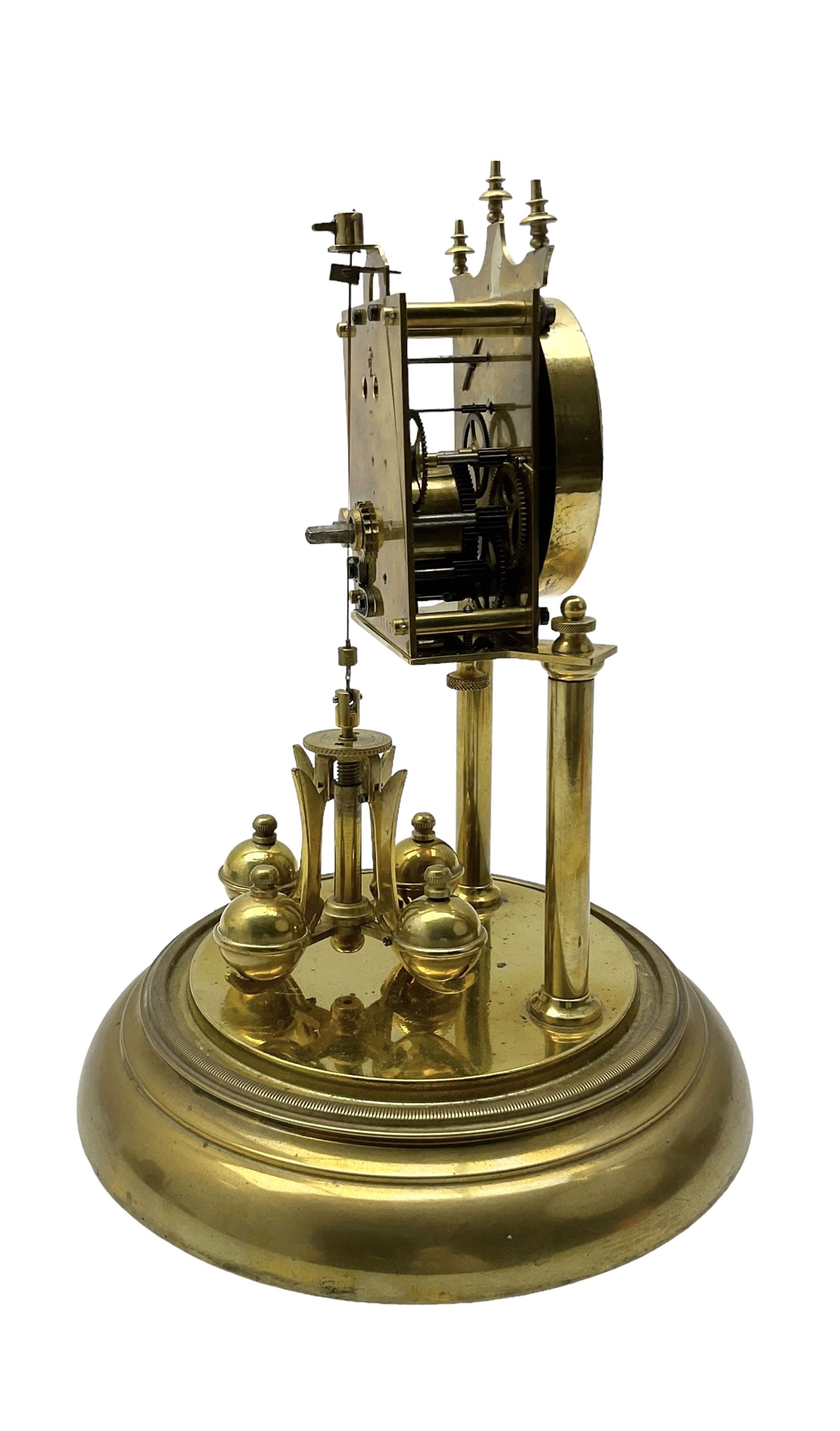 Continental- early-20th century torsion clock under a glass dome, movement raised on two pillars on a circular brass base, with an enamel dial, Roman numerals and spade hands, oscillating four ball circular pendulum. Torsion spring intact.