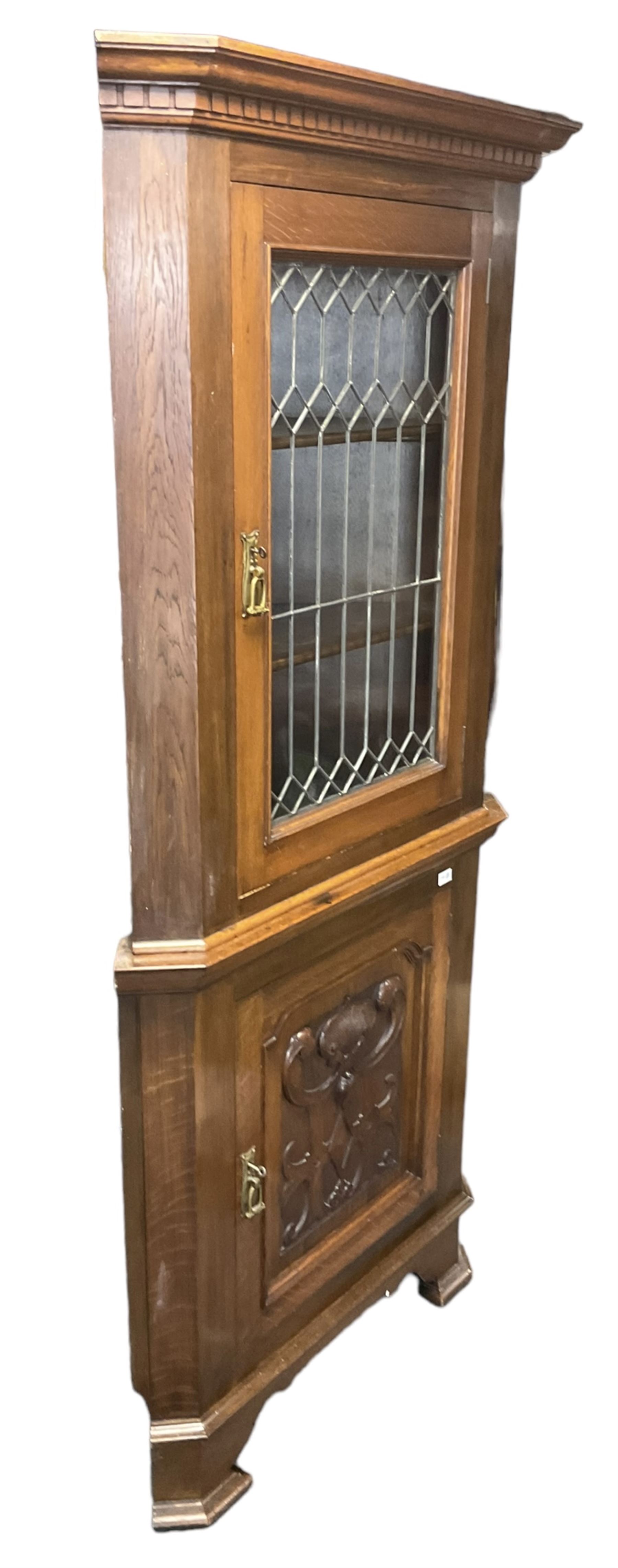 Arts & Crafts period oak corner cabinet, projecting cornice over astragal glazed door and single panelled door decorated with applied carved foliate scrolls and stylised roods surrounded by moulded edge, enclosing single shelf