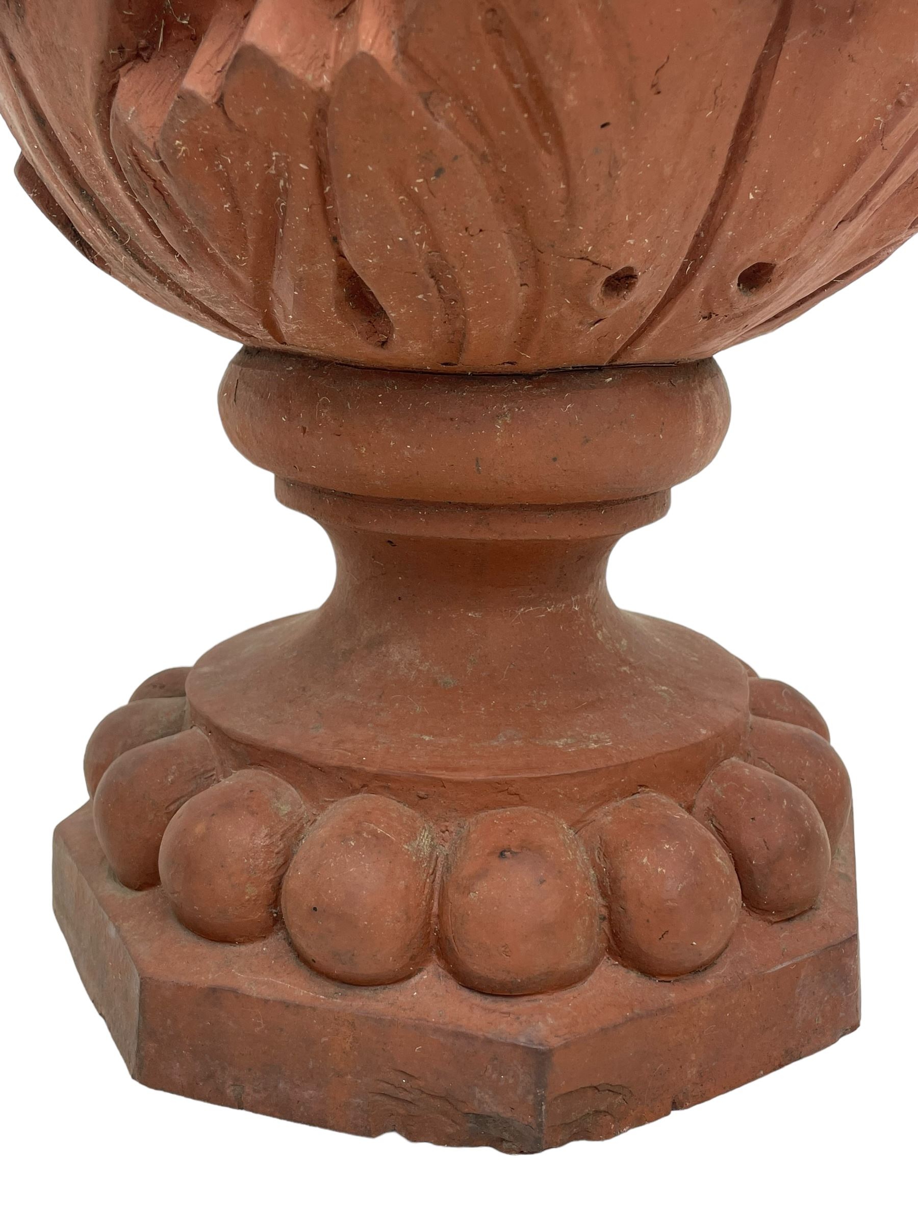 Pair of late 19th to early 20th century red terracotta garden urn planters, the shallow bowls moulded with curled acanthus leaf decoration, on circular foot with globular beaded moulding, octagonal base