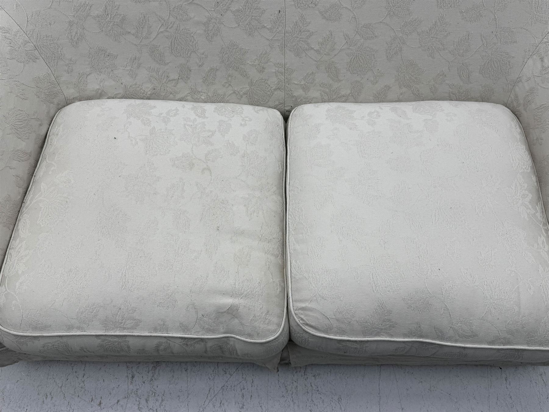 Two-seat traditionally shaped sofa, upholstered in pale floral pattern fabric, with additional covers