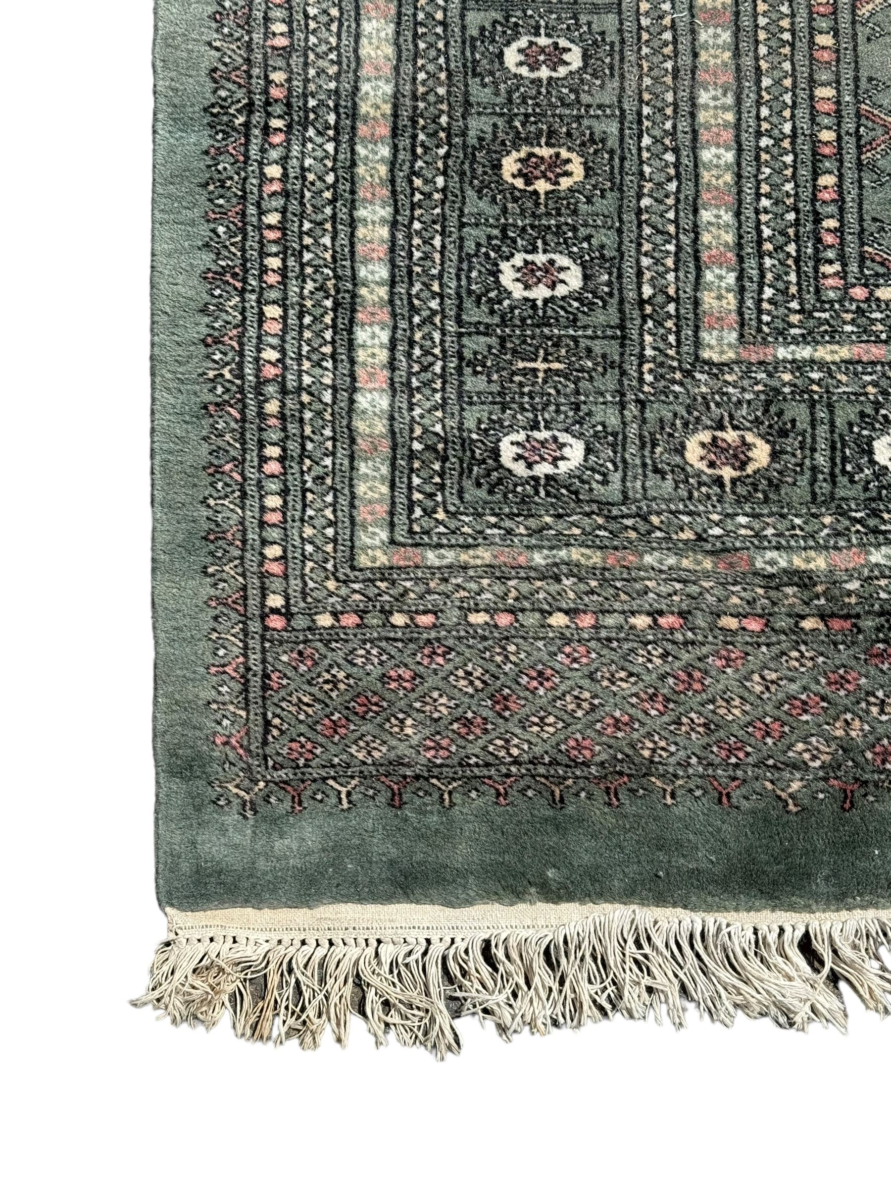 Pakistani Bokhara green ground rug, the field decorated with rows of repeating gul motifs, the main border featuring a series of smaller gul designs and geometric patterns, framed by multiple guard stripes