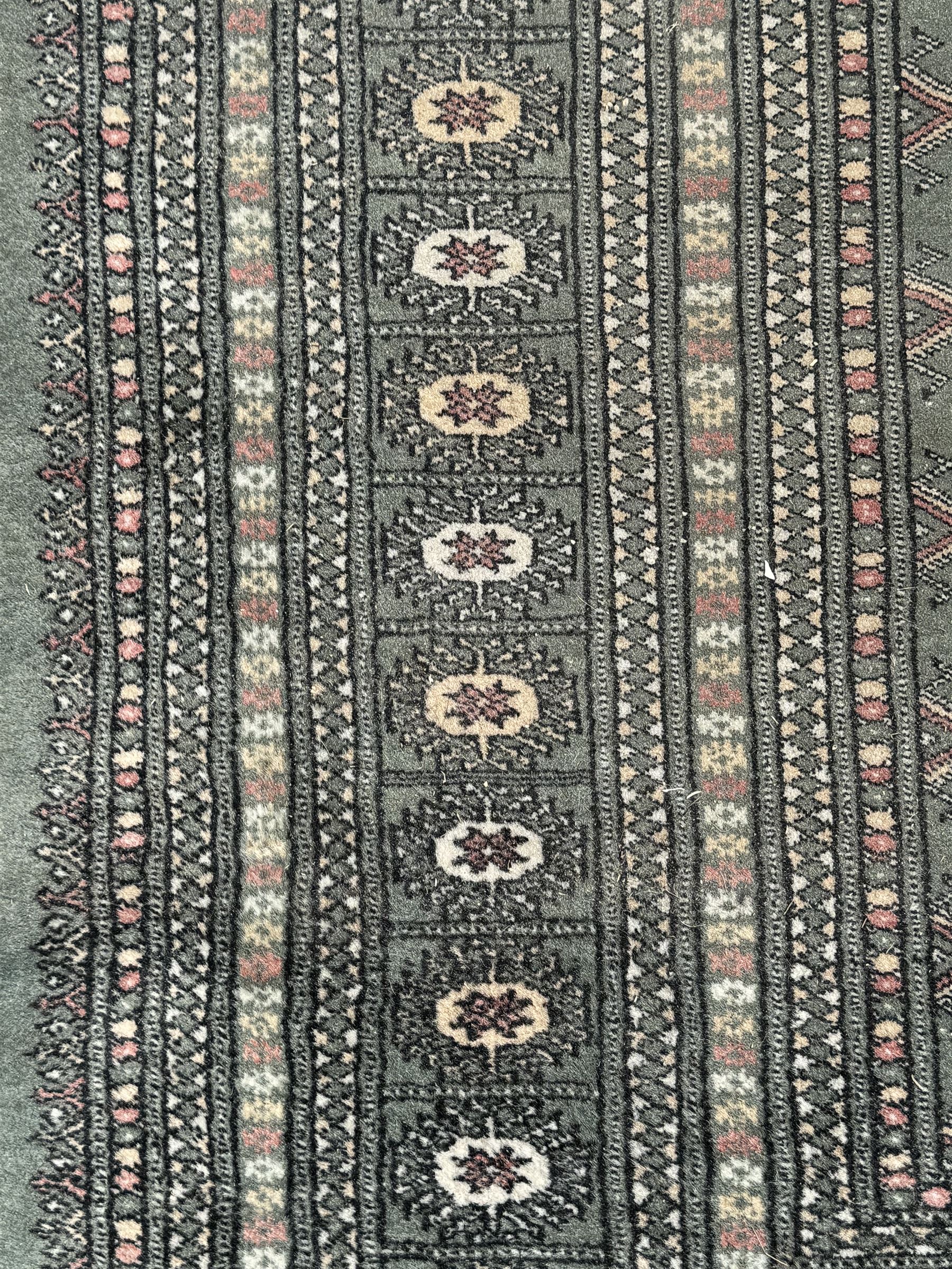 Pakistani Bokhara green ground rug, the field decorated with rows of repeating gul motifs, the main border featuring a series of smaller gul designs and geometric patterns, framed by multiple guard stripes