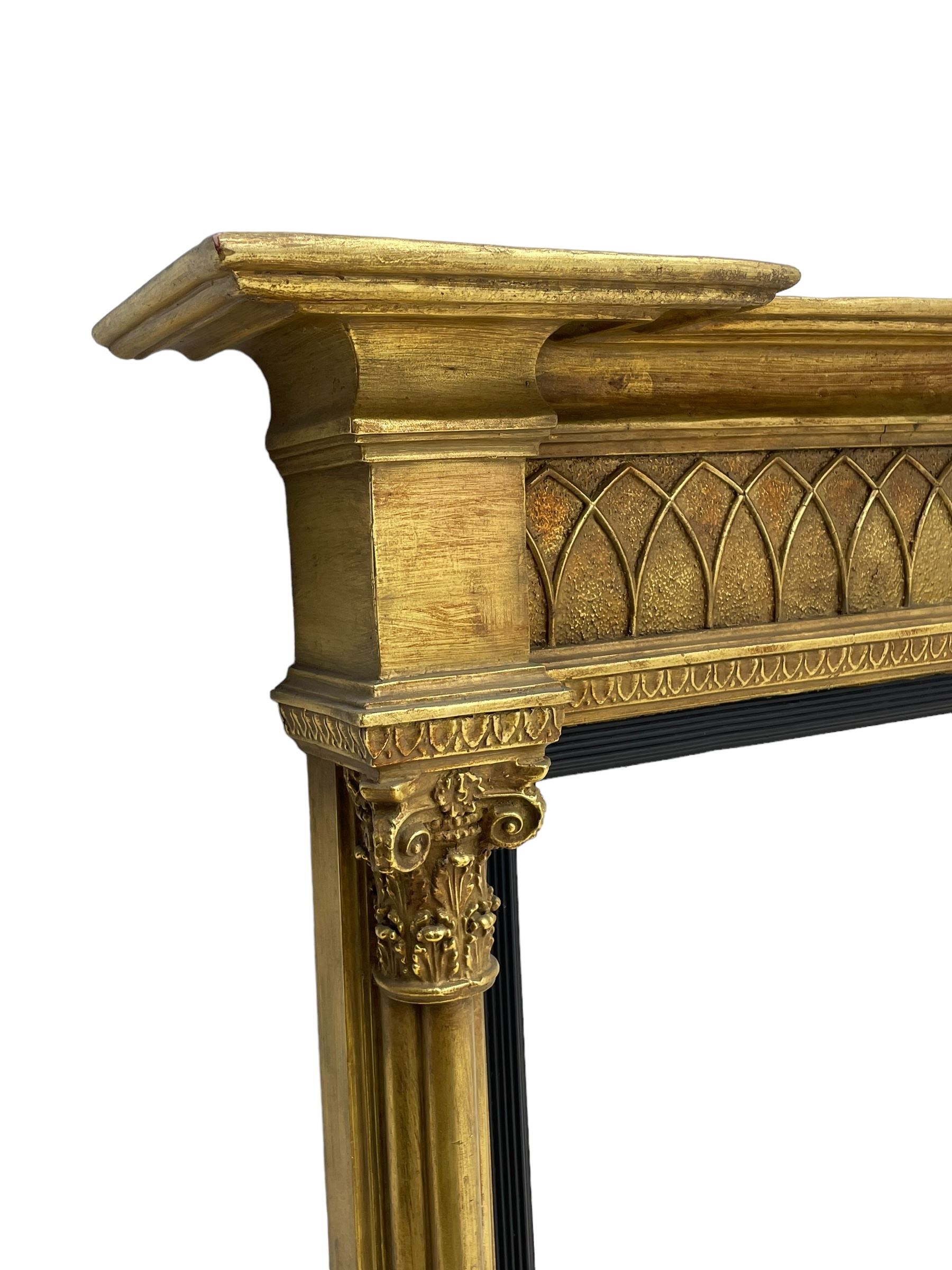 Regency design giltwood overmantel mirror, projecting cornice over pointed arcade frieze and foliate moulded upper edge, plain mirror plate within reed moulded ebonised slip, flanked by cluster columns with acanthus and scroll decorated Composite order capitals 