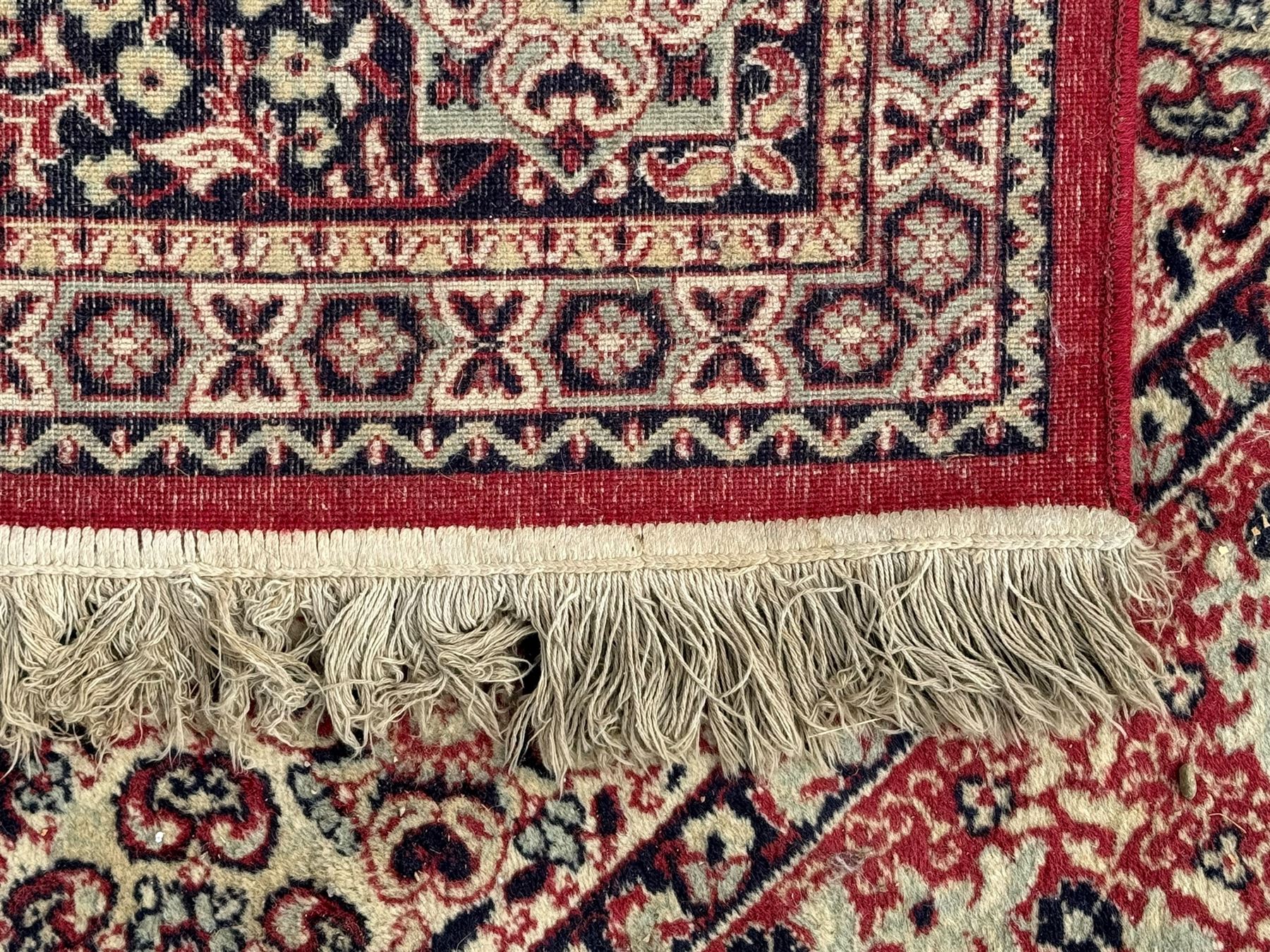 Persian Heriz design red ground carpet, the field decorated with a central star-shaped medallion surrounded by geometric floral motifs and angular vine patterns, the spandrels highlighted with palmette designs, the main border featuring a series of stylised rosettes and leaves against a dark blue ground, enclosed by multiple guard stripes with alternating floral and geometric motifs