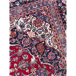 Large Persian Kashan crimson ground carpet, central floral medallion surrounded by swirling leafy branches and palmettes, enclose by floral pattern spandrels, the indigo border with overall scrolling design decorated with palmettes, within guard stripes 