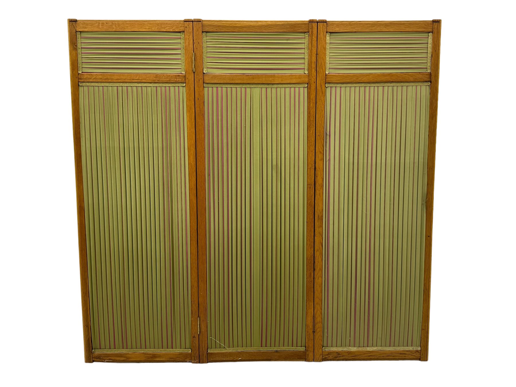 Edwardian oak and fabric folding screen, featuring three panels with oak frames, one side covered in green striped fabric with decorative trim, the reverse side in pink moiré effect fabric, connected by brass hinges