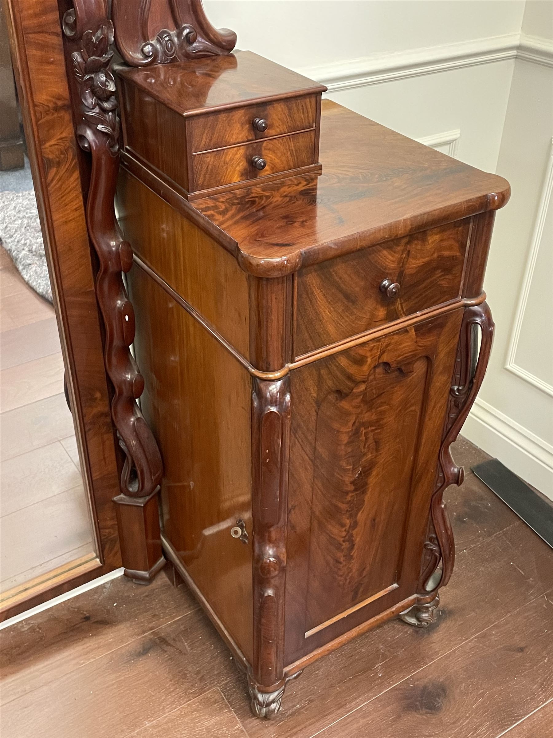 Tall Victorian figured mahogany twin pedestal dressing table, the tall mirror with flower head and scrolled leaf carved pediment, flanked by two turned and carved finials over faceted lancet arched lantern tops, plane mirror plate enclosed by shaped frame, pierced and undulating moulded uprights, on C-scroll and curled leaf carved supports fitted with cast brass hinged candle sconces, each pedestal fitted with two small trinket drawers over larger drawer and panelled cupboard, canted corners with matched upright mounts, the cupboard doors enclosing slides, on scroll carved feet 