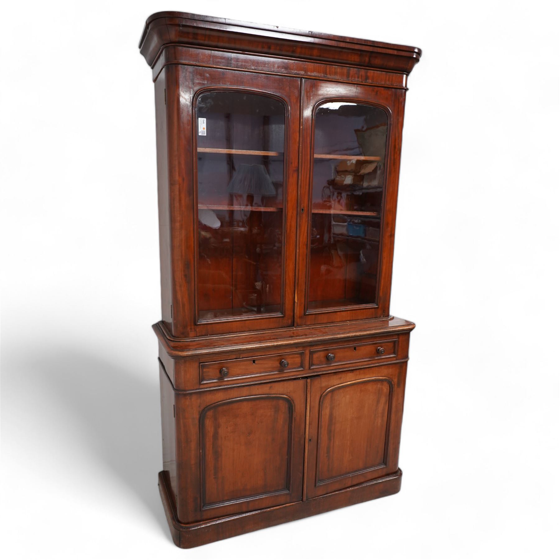 Victorian mahogany bookcase on cupboard, projecting cornice over two glazed doors, the lower section fitted with two drawers and two panelled cupboards, on moulded plinth base 