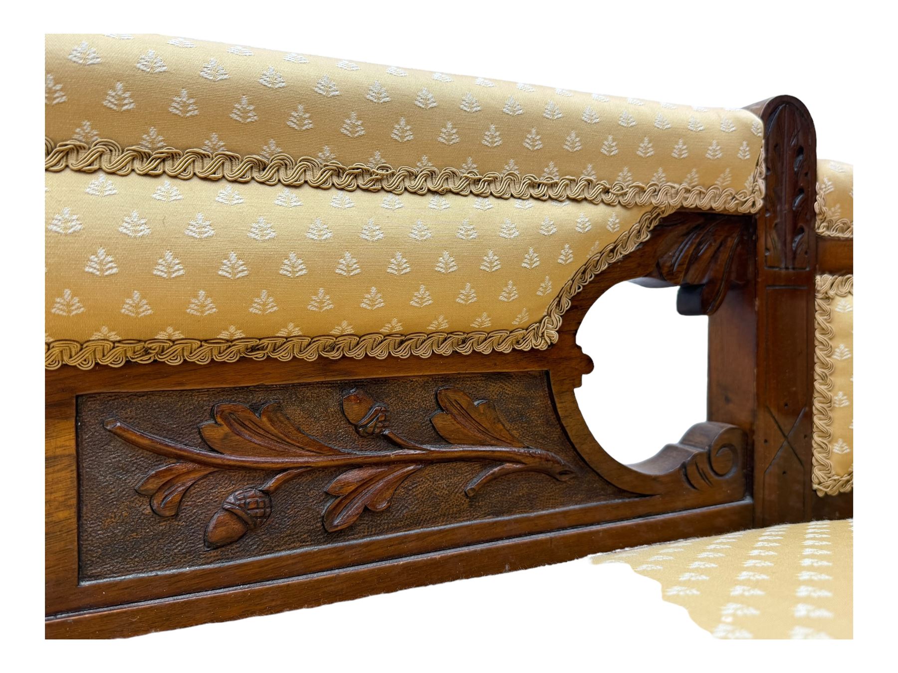 Late Victorian walnut framed chaise longue, scrolled backrest and sides upholstered in patterned yellow fabric, carved floral motifs to the backrest and sides, raised on turned supports with castors