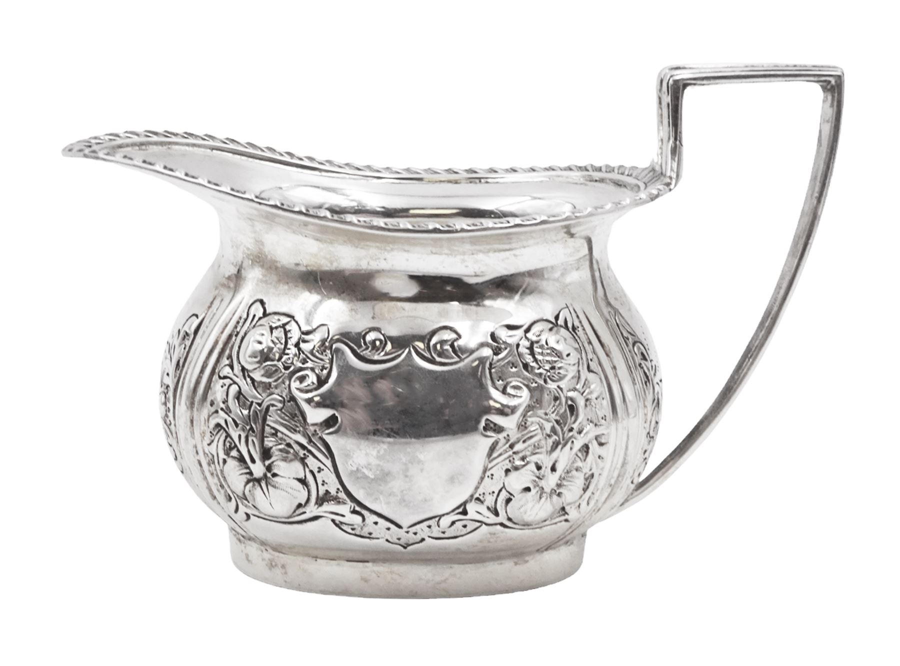 Edwardian silver milk jug, of helmet form with angular handle and oblique gadrooned ring, embossed with floral decoration and blank shield shaped cartouche, H8cm