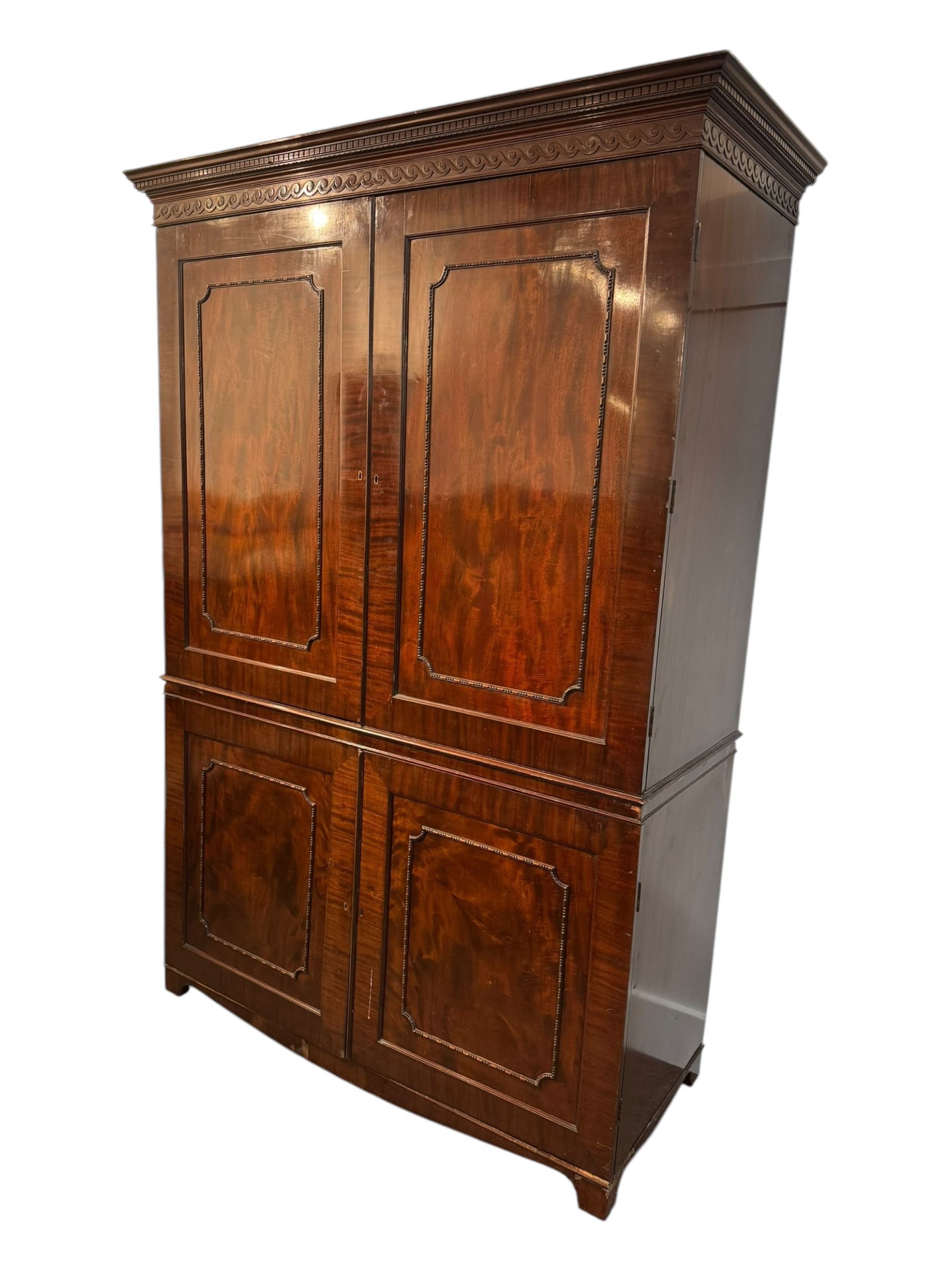 Victorian mahogany linen press, projecting cornice with dentil and scroll detailing, double panelled doors opening to an interior fitted with a brass hanging rail and coat hooks, lower section with two drawers and fitted shelves for additional storage, raised on bracket feet