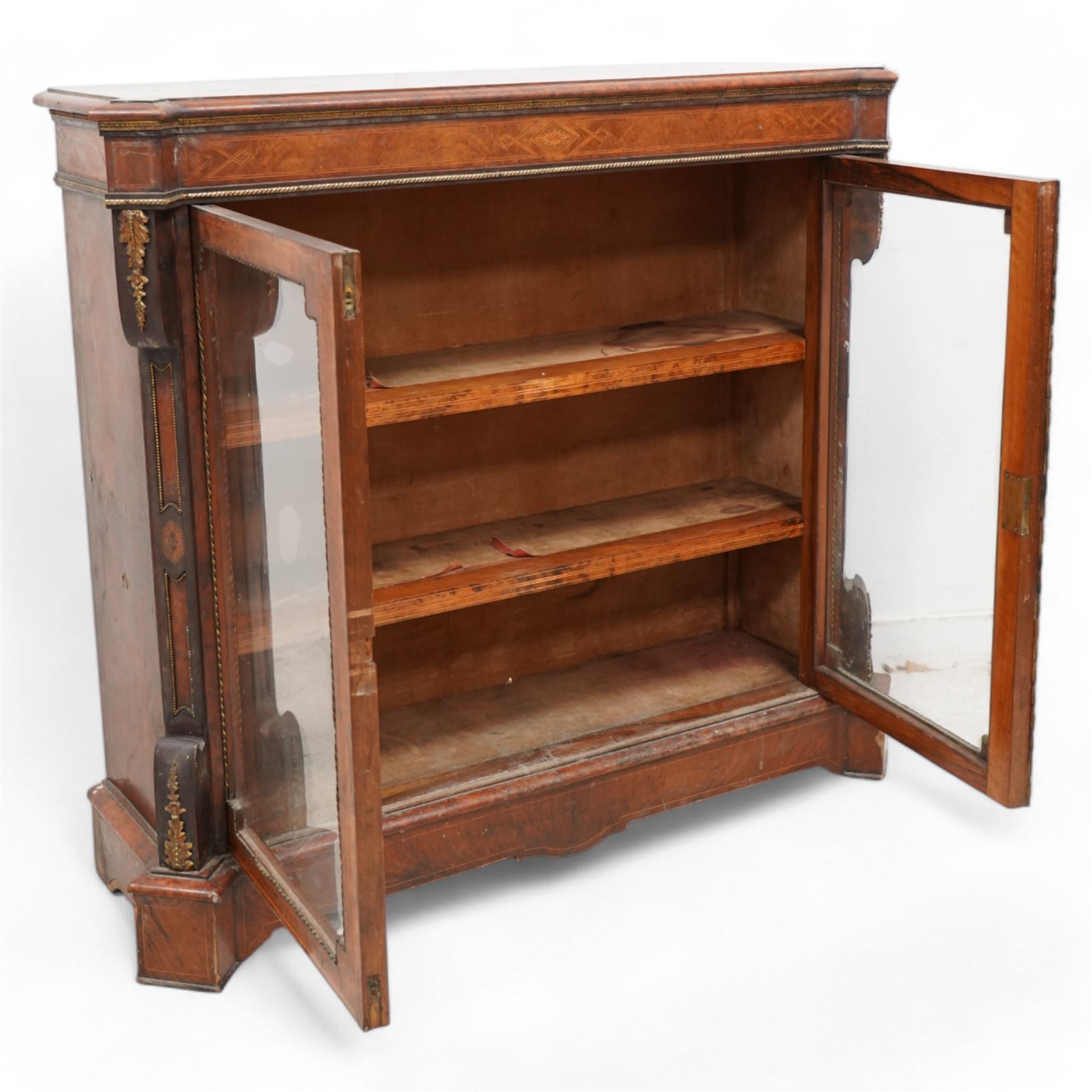 Victorian inlaid walnut and gilt metal mounted pier display cabinet, moulded rectangular top with extending square corners, the frieze inlaid with geometric satinwood bands and decorated with gilt metal edging, two glazed doors enclosing two shelves, enclosed by canted corners with recessed panels and gilt metal mounts, on moulded skirt base 