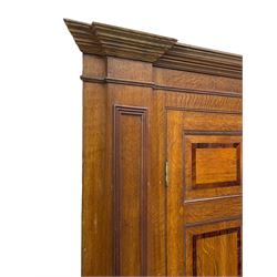 George III and later oak and mahogany banded corner cupboard, moulded cornice over four panelled doors, the door panels inlaid with mahogany bands, projecting square pilasters throughout with applied reeded mouldings, the painted interior fitted with shaped shelves, on moulded plinth base 