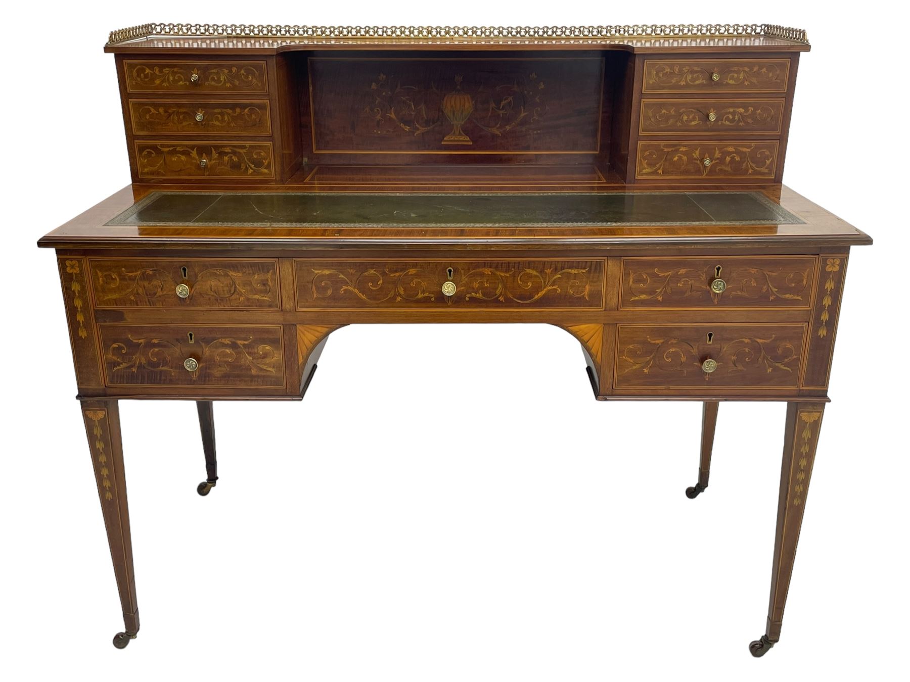 Edwardian inlaid mahogany writing desk, raised galleried back over inlaid central urn with scrolling leafy branches and six small drawers, satinwood banded rectangular moulded top with tooled leather inset, fitted with five drawers, the drawer facias inlaid with scrolling foliage and satinwood banding, square tapering supports inlaid with trailing bell flowers, on brass and ceramic castors 