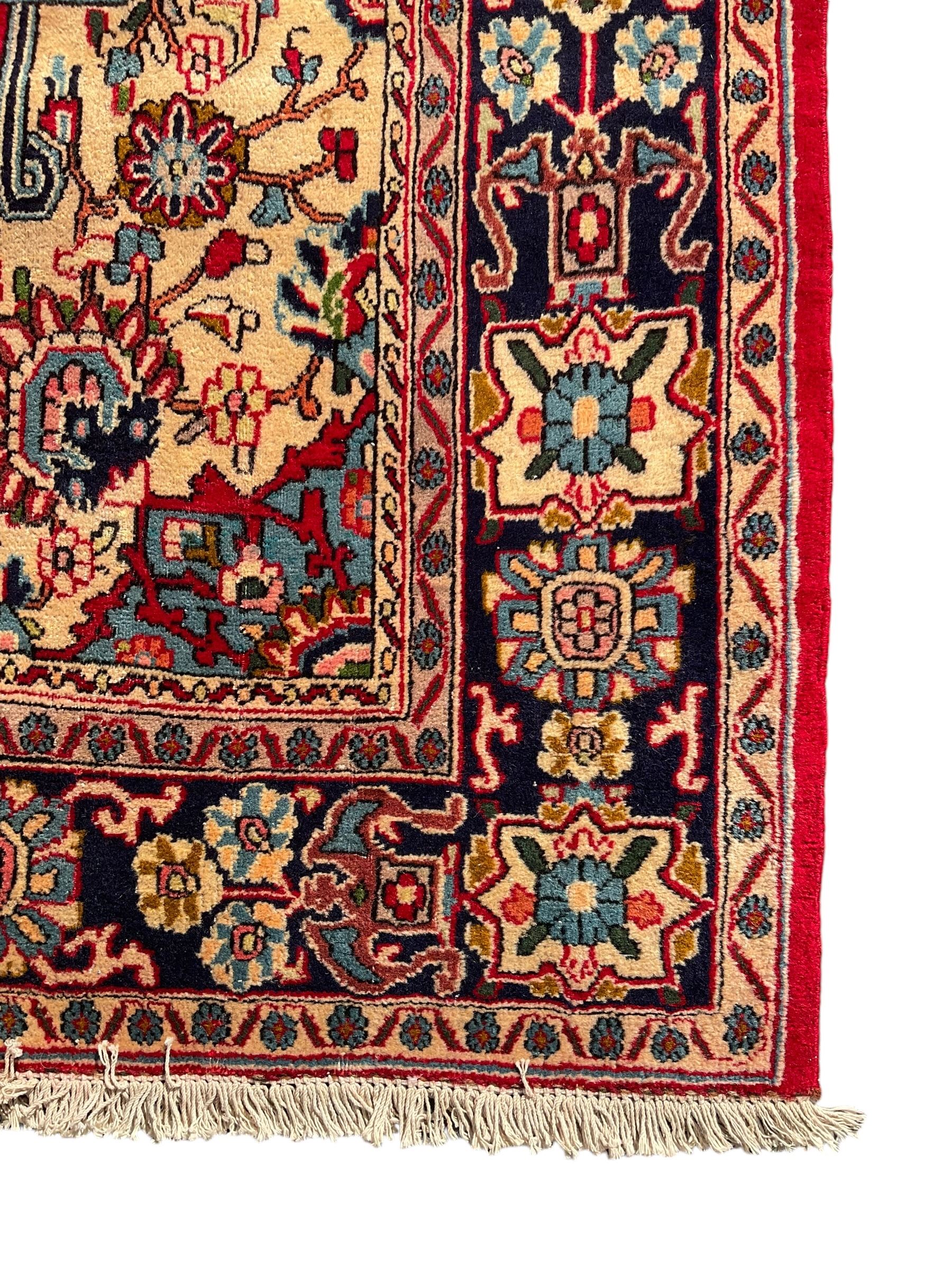 Central Persian Isfahan crimson ground carpet, central floral medallion in ivory and blue, set within a field of dense floral patterns, bordered by a navy band decorated with stylised flower heads and vines