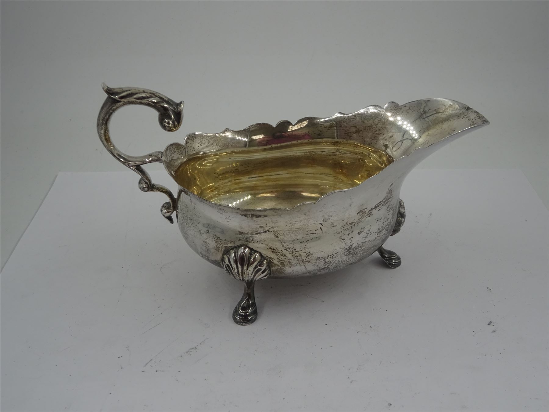 1930s silver sauce boat, of typical form with shaped rim, and acanthus leaf capped flying scroll handle, upon three palmette mounted stepped feet, hallmarked 	Harrods Ltd, London 1934, including handle H10.4cm